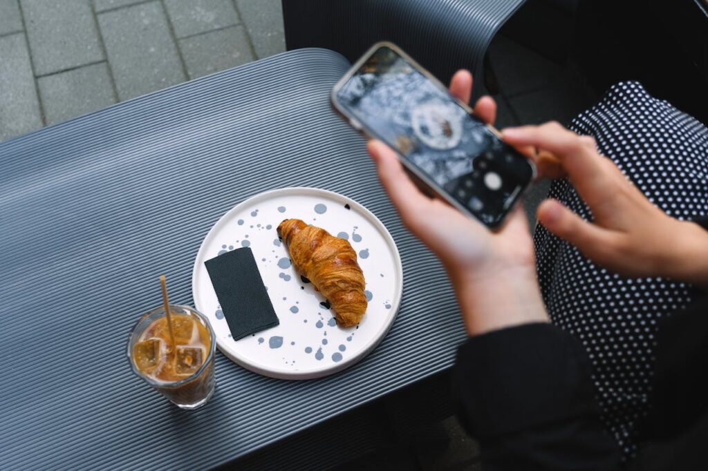 Close-up of a croissant and iced coffee on a terrace table, captured with a smartphone.