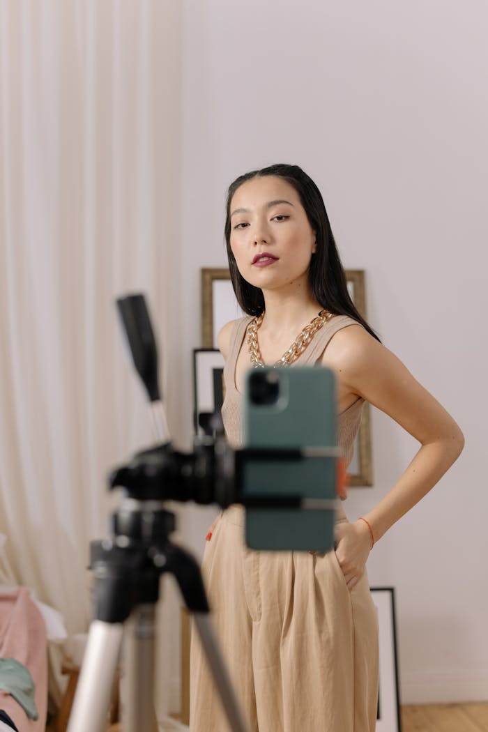 Stylish woman filming content with smartphone on tripod indoors.