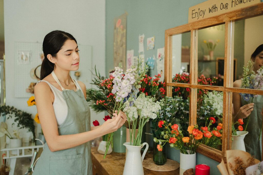 A female florist arranging a bouquet in a cozy floral shop with a variety of blooms.